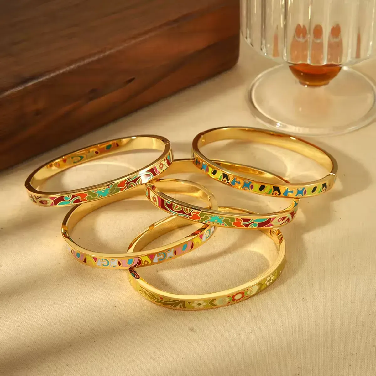 Bracelets joncs dorés avec motifs émail colorés posés sur une table